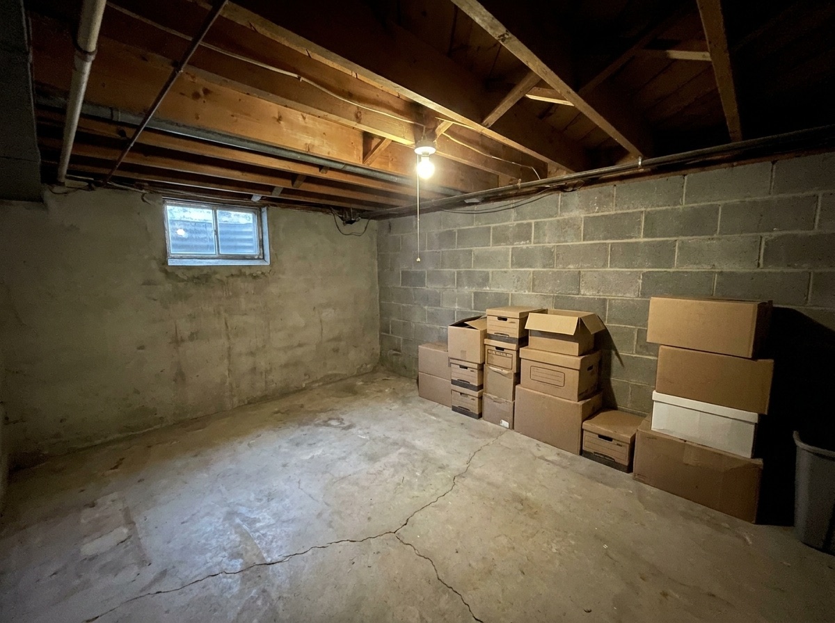 Unfinished basement with bare concrete and exposed framing before finishing